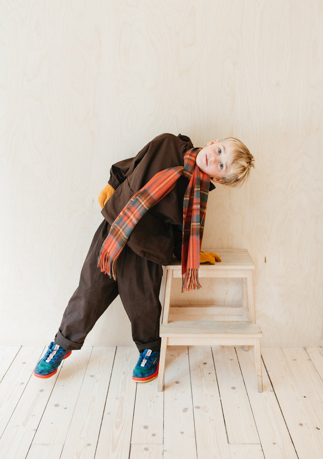 Young child wearing TBCo Lambswool Kids Scarf in Stewart Royal Antique Tartan with brown outfit on wooden steps