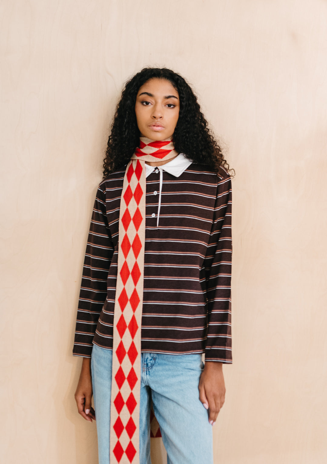 Model wearing TBCo Merino Wool Skinny Scarf in Red Harlequin with red and oatmeal diamond pattern and long slim fit