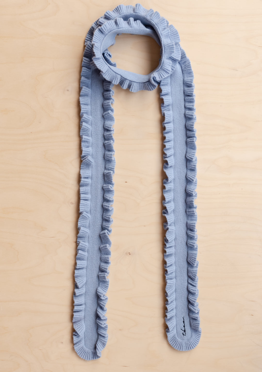 TBCo Merino Wool Skinny Scarf in Blue Ruffle laid flat on wooden surface showing ruffled edges and soft texture