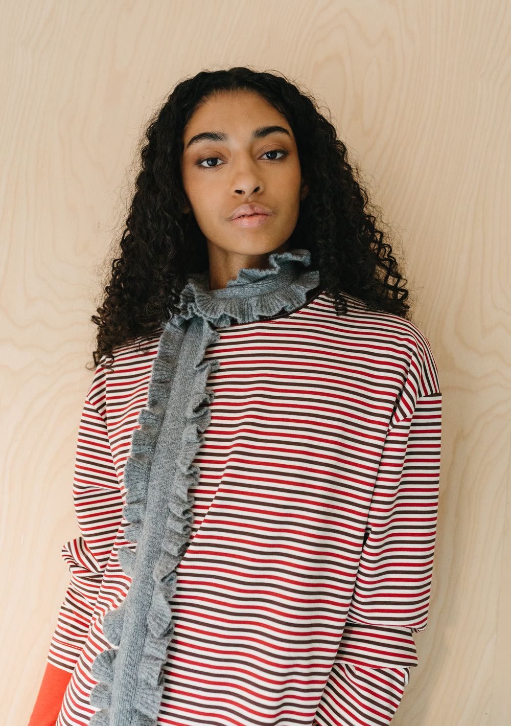 Model wearing TBCo Merino Wool Skinny Scarf in Grey Ruffle with soft ruffled edges over striped top on wood background