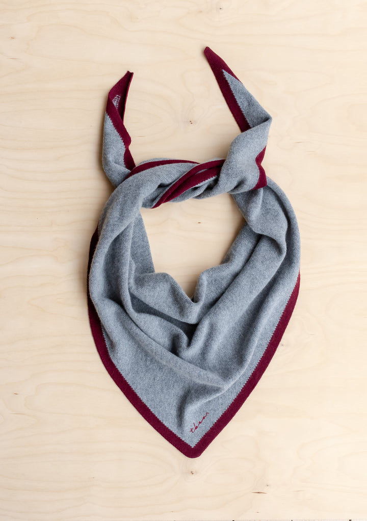 TBCo Large Merino Wool Triangle Scarf in Charcoal & Burgundy, featuring a light grey body, burgundy tipped border, and a loose knot on a wood surface.