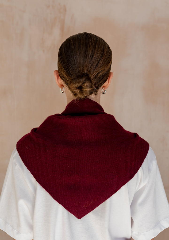 TBCo Merino Wool Triangle Scarf in Burgundy draped over shoulders, featuring embroidered logo, paired with white t-shirt and silver hoop earrings.