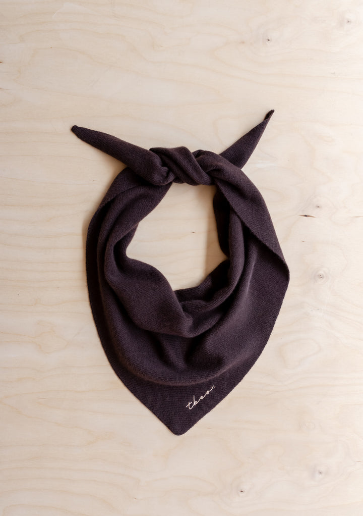 TBCo Merino Wool Triangle Scarf in Brown, featuring a knotted design and embroidered logo, laid on wood surface, showcasing its softness and versatile styling.