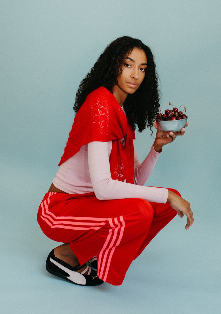 Model wearing TBCo Large Merino Wool Triangle Scarf in Red Pointelle draped over shoulders holding bowl of cherries