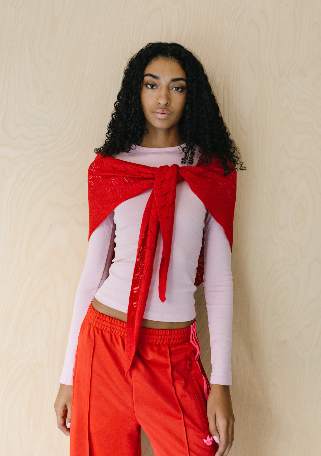 Model wearing TBCo Large Merino Wool Triangle Scarf in Red Pointelle tied at front over light pink top and red trousers