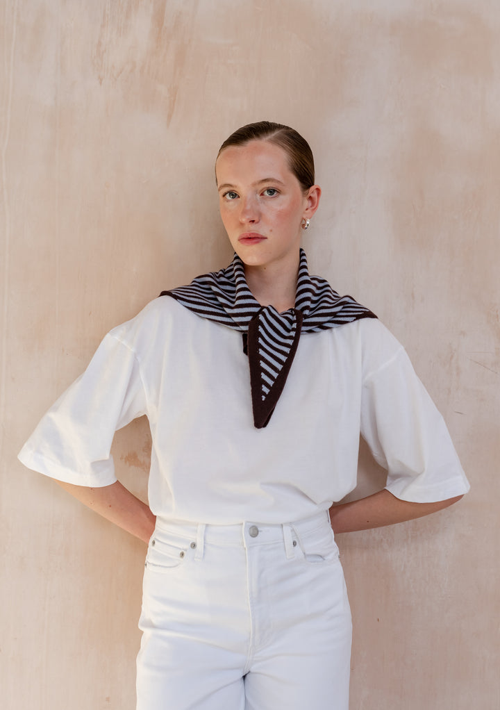 Woman wearing TBCo Merino Wool Triangle Scarf in Blue & Brown Stripe, draped over white outfit, showcasing its lightweight design and versatile tie options.