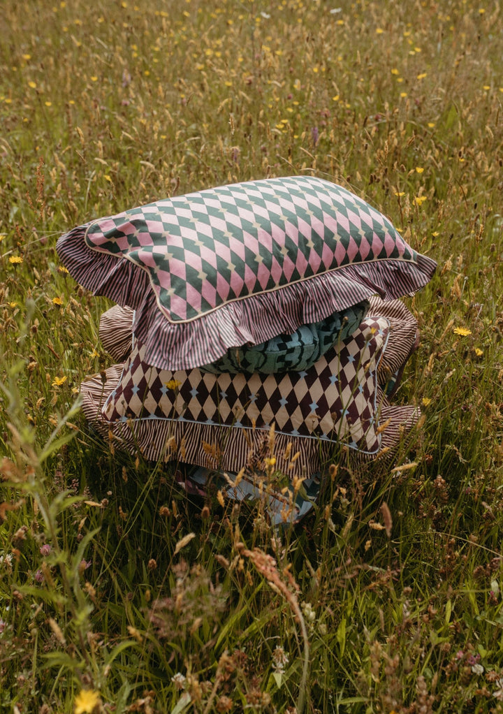 Stack of patterned cushions in a wildflower meadow showcasing the Mix & Match Cushion Set by TBCo with sustainable cotton covers