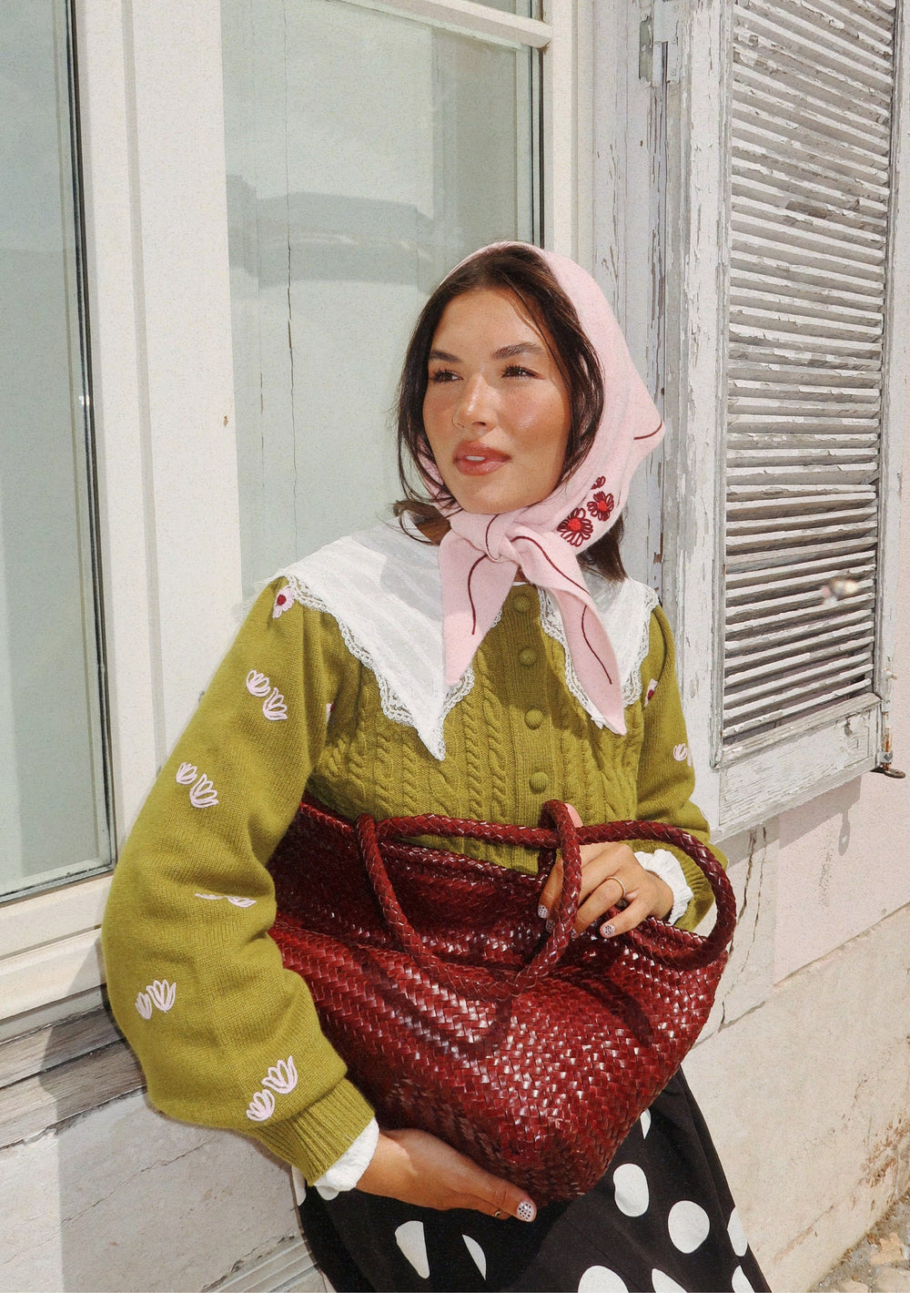 Woman wearing NC x TBCo Pink Floral Wool Triangle Scarf styled with green knitwear and red woven bag outdoors