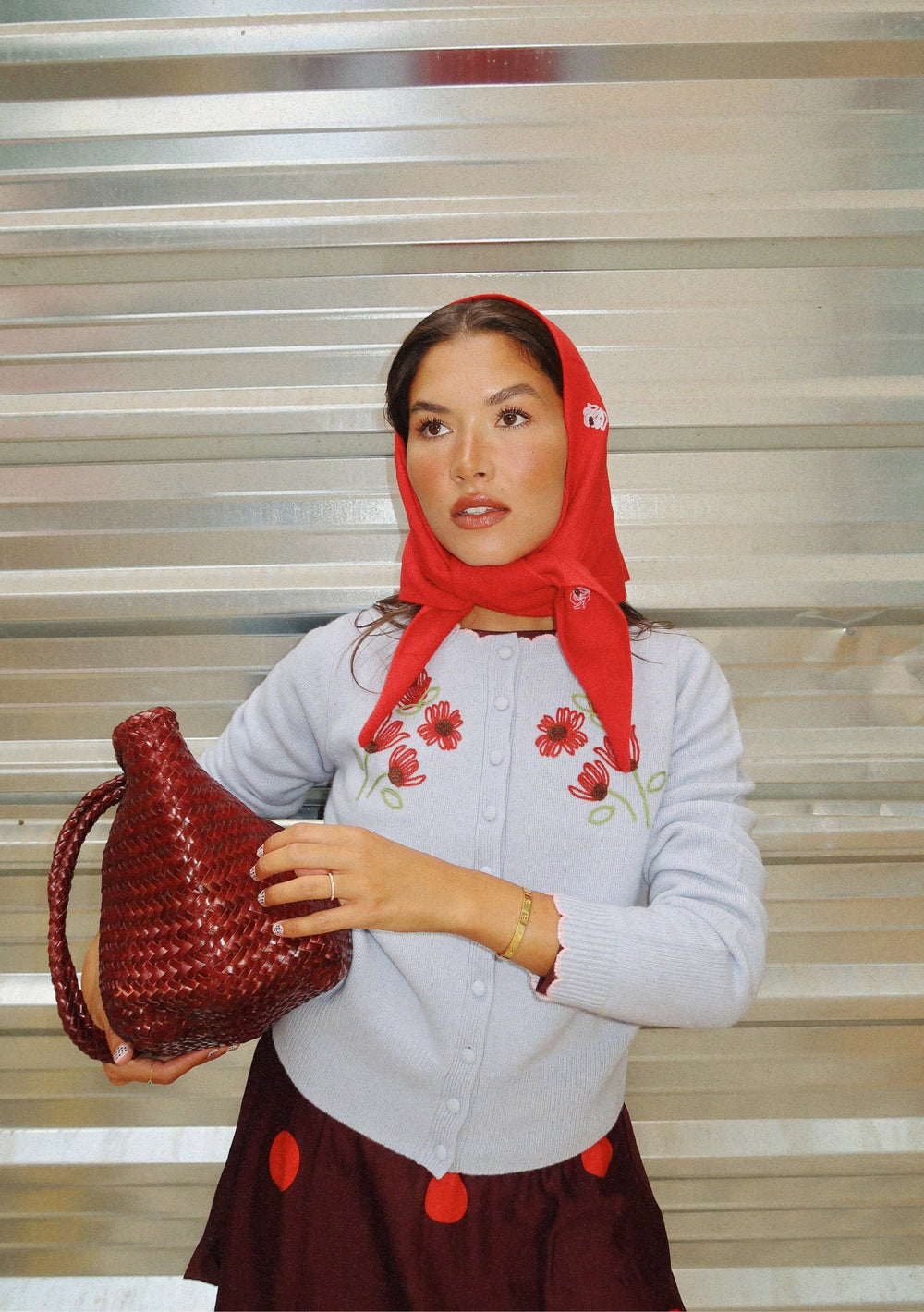 Woman wearing a red NC x TBCo Red Floral Wool Triangle Scarf styled as a headscarf with embroidered cardigan and wicker bag