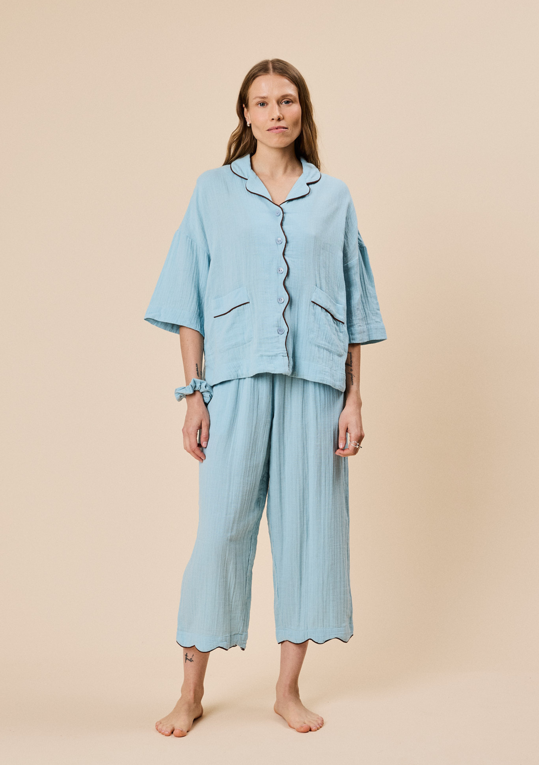 Woman wearing TBCo Cropped Cotton Pyjamas in Blue with contrast trim and loose wide-leg trousers on neutral background