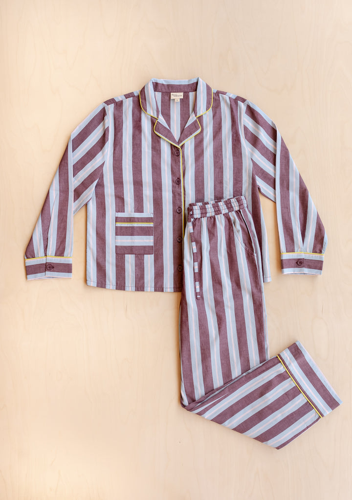 TBCo x Glassette Cotton Pyjamas in Berry Stripe, featuring a button-front shirt and elastic waist pants with contrasting piping and dual pockets, laid flat on wood.