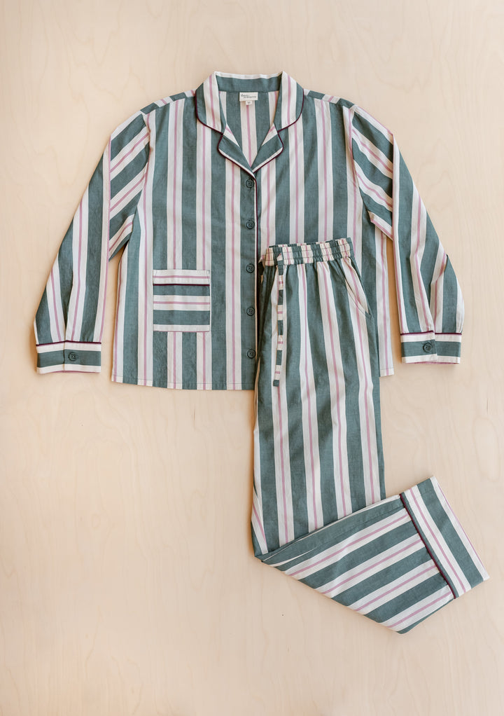 TBCo x Glassette Cotton Pyjamas in Green Stripe, featuring a button-front shirt and drawstring pants with burgundy piping, laid on a light wood surface.