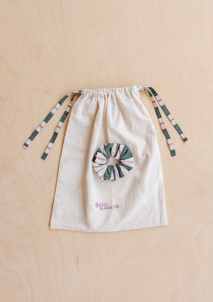 Natural-canvas drawstring pouch with striped ties and matching scrunchie, stamped tbco x GLASSETTE, from TBCo x Glassette Cotton Pyjamas in Green Stripe collection.