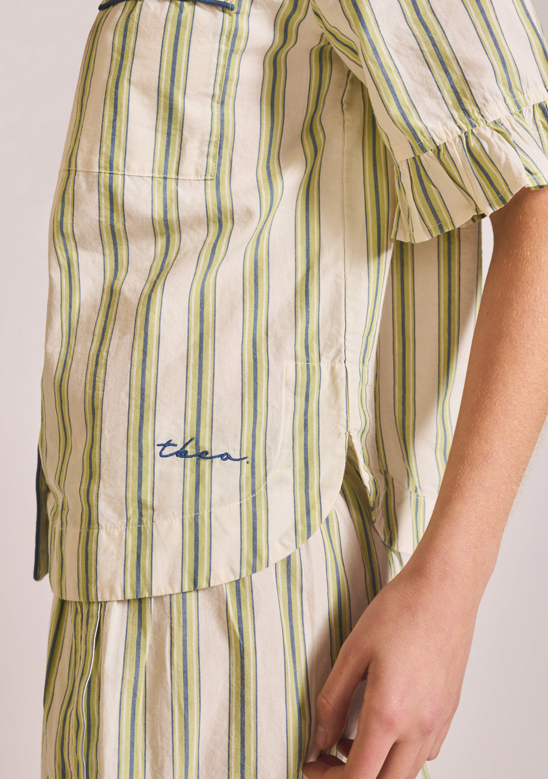 Close-up portrait of TBCo Cotton Pyjamas in Olive Stripe Ruffle showing embroidered logo and ruffled sleeve detail