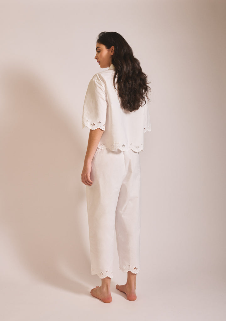 Woman seen from behind wearing TBCo Cropped Cotton Pyjamas in White Shell with scalloped eyelet trim on sleeves and trousers