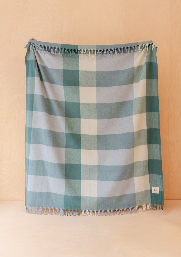 Recycled Wool Blanket in Blue Bold Check by TBCo hanging flat against pale wood with soft fringed edges visible