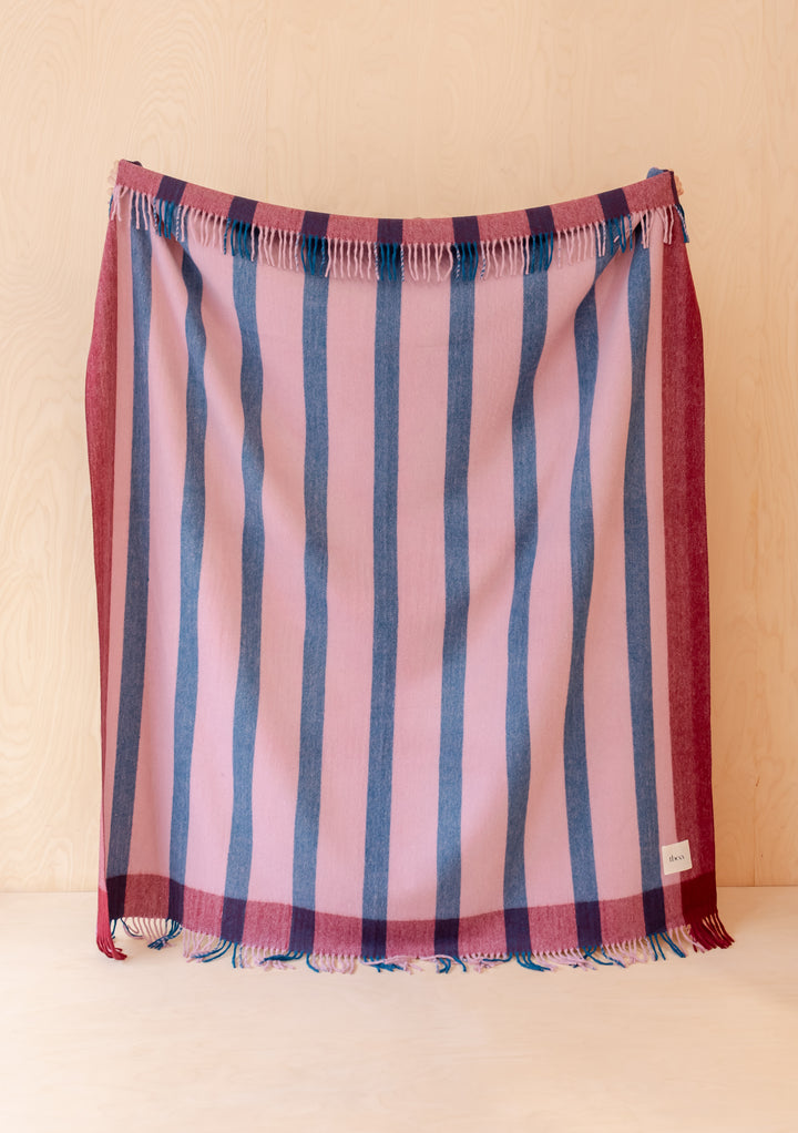 TBCo Recycled Wool Blanket in Berry Frame Stripe with vertical blue and berry stripes and fringed edges on light wood background
