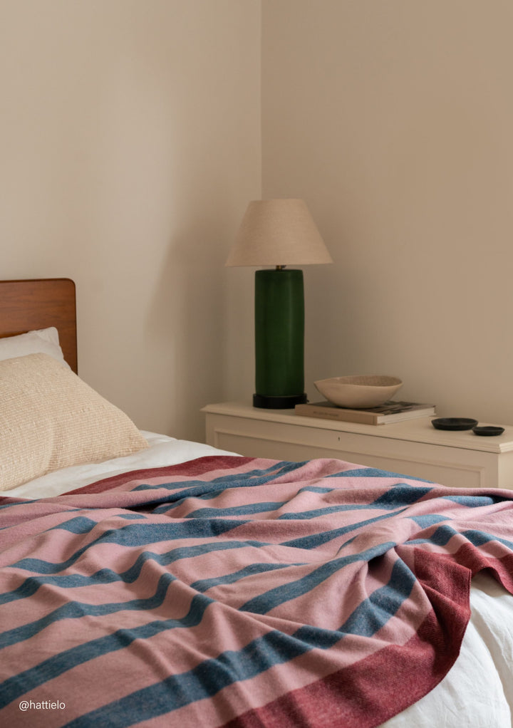 TBCo Recycled Wool Blanket in Berry Frame Stripe laid on bed with soft natural light and textured cushion nearby