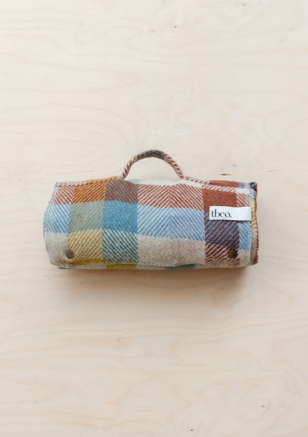TBCo Recycled Wool Small Picnic Blanket rolled up in rainbow herringbone check pattern with carrying handle, showcasing multicoloured squares