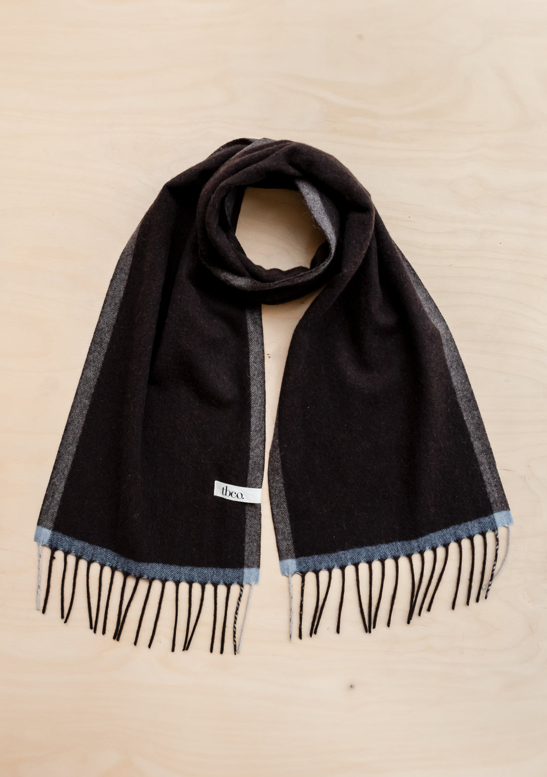 TBCo Cashmere & Merino Scarf in brown with grey and blue contrast edges, featuring fringed ends laid flat on beige surface