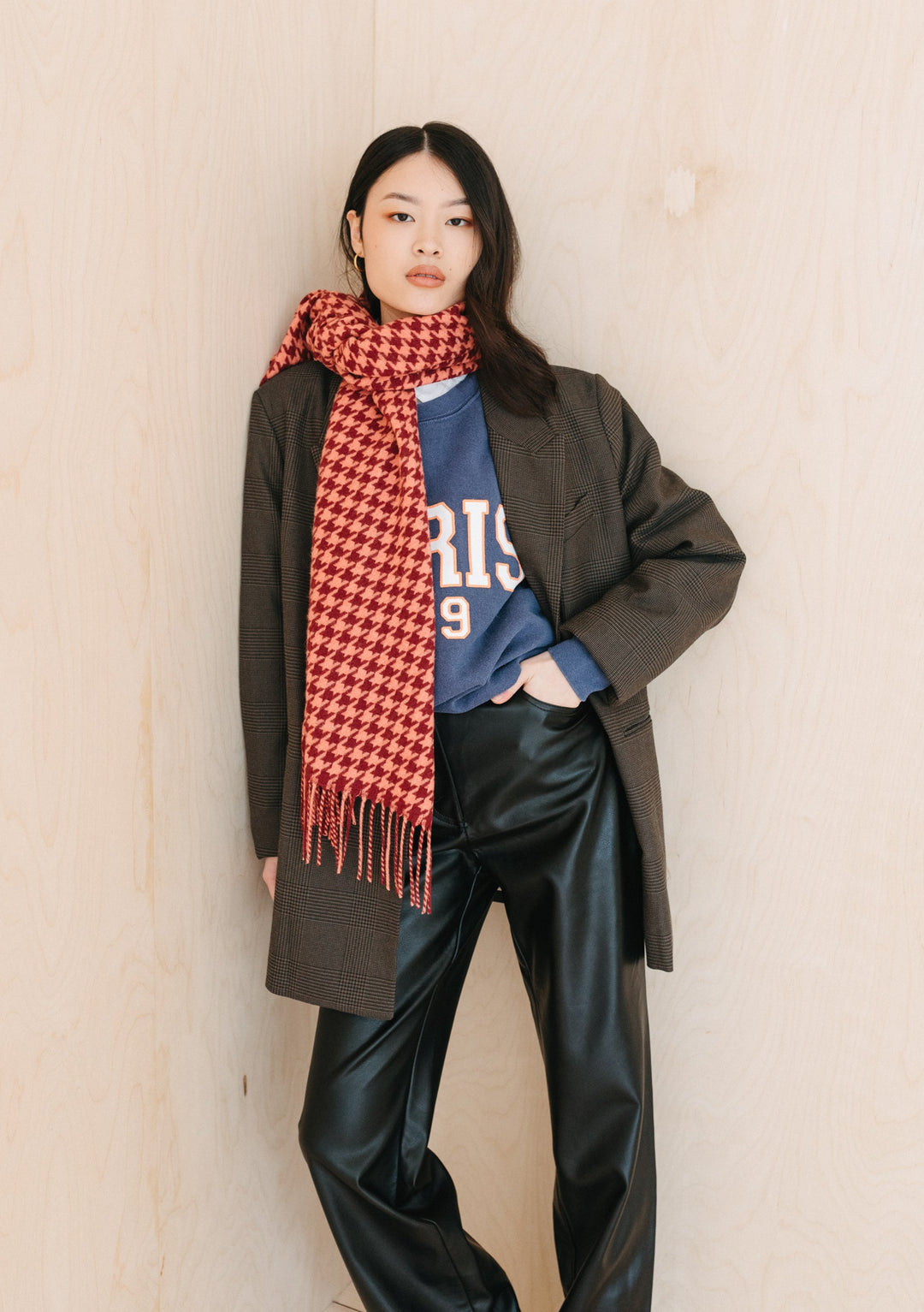 Person wearing TBCo's Lambswool Oversized Scarf in Berry Houndstooth draped over dark coat with fringed detail and houndstooth pattern
