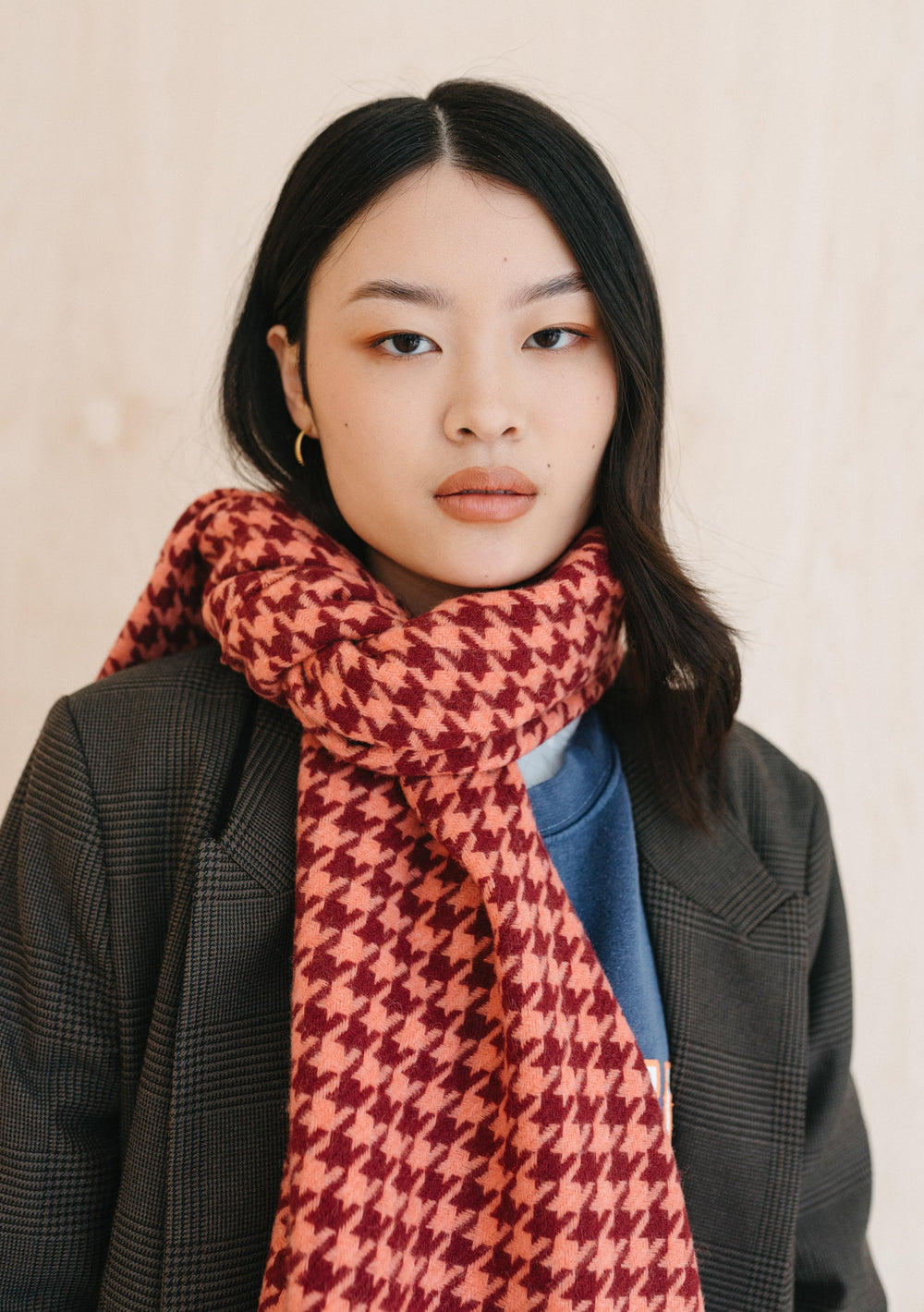 A person wearing TBCo's Lambswool Oversized Scarf in Berry Houndstooth draped stylishly with a grey blazer and blue top