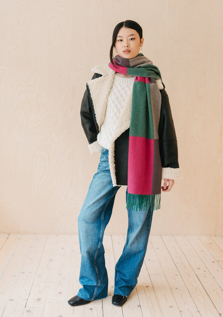 Model wearing TBCo Lambswool Oversized Scarf in Block Jacquard featuring green and fuchsia colour blocks with fringe detail