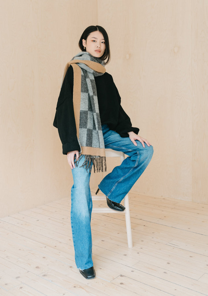 TBCo Lambswool Oversized Scarf in Checkerboard Jacquard styled on model with black sweater and jeans, showing grey and camel pattern