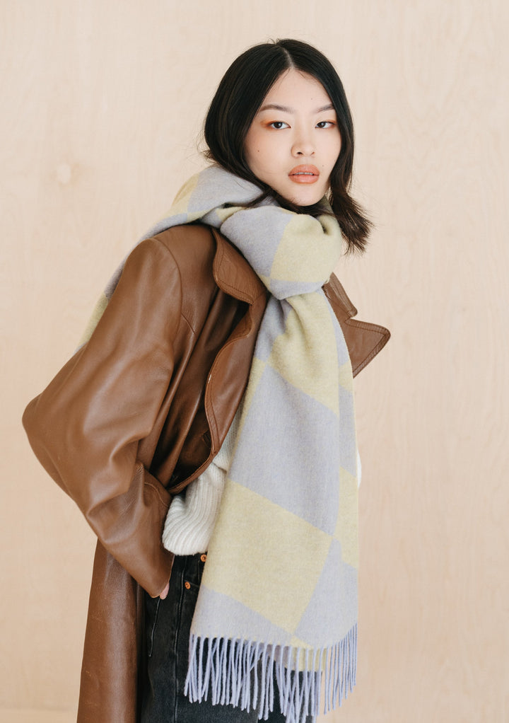 TBCo lambswool oversized scarf in organic jacquard pattern styled with brown leather trench coat against beige backdrop