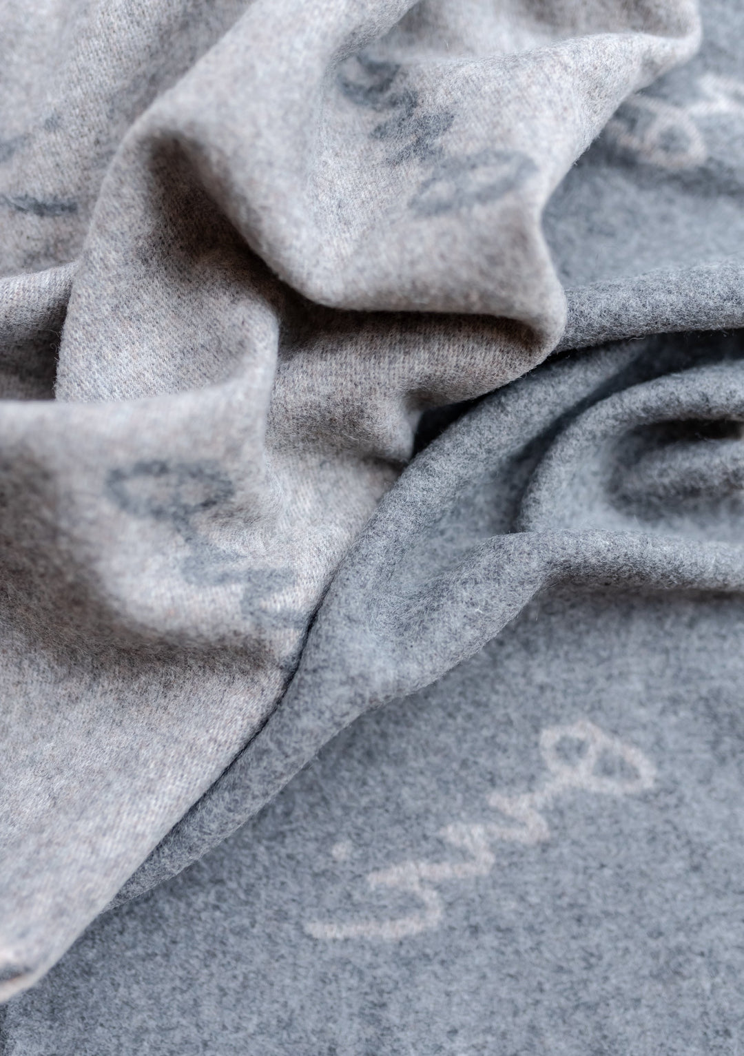Close-up detail of TBCo x Pretty Little Fawn Oui Scarf in soft grey lambswool showing delicate text pattern and fabric texture