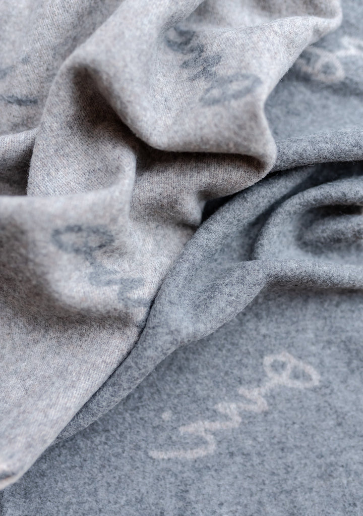Close-up detail of TBCo x Pretty Little Fawn Oui Scarf in soft grey lambswool showing delicate text pattern and fabric texture