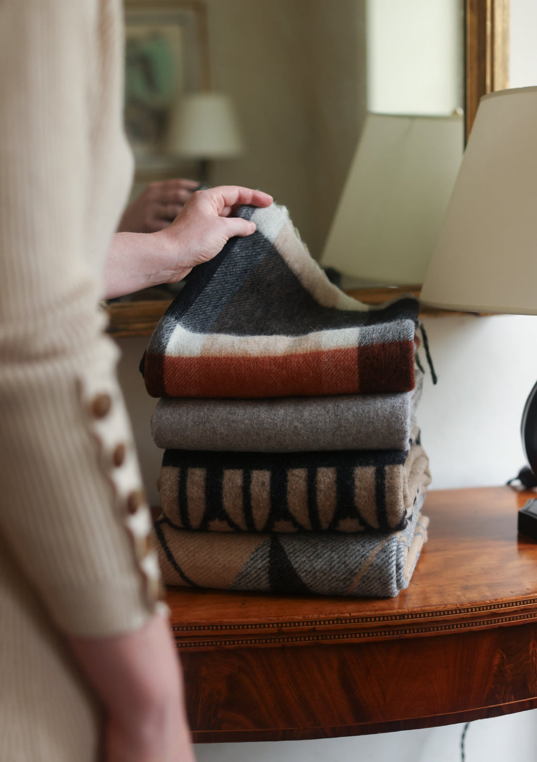 Neatly folded stack of TBCo x Pretty Little Fawn Oui wool scarves in neutral colours displayed on wooden furniture