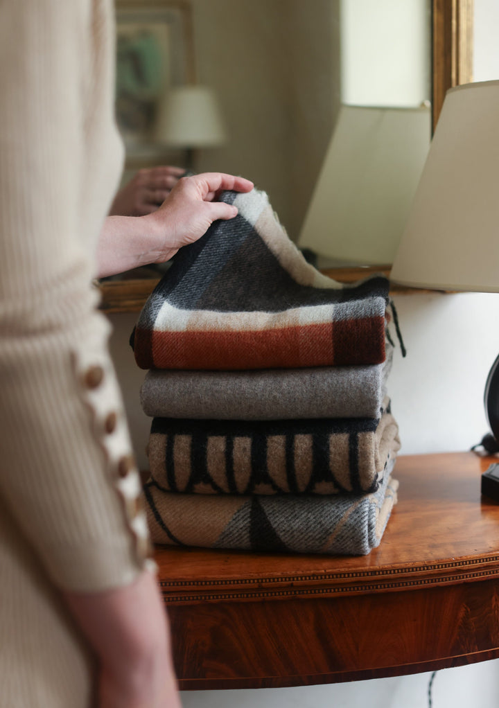 Neatly folded stack of TBCo x Pretty Little Fawn Oui wool scarves in neutral colours displayed on wooden furniture