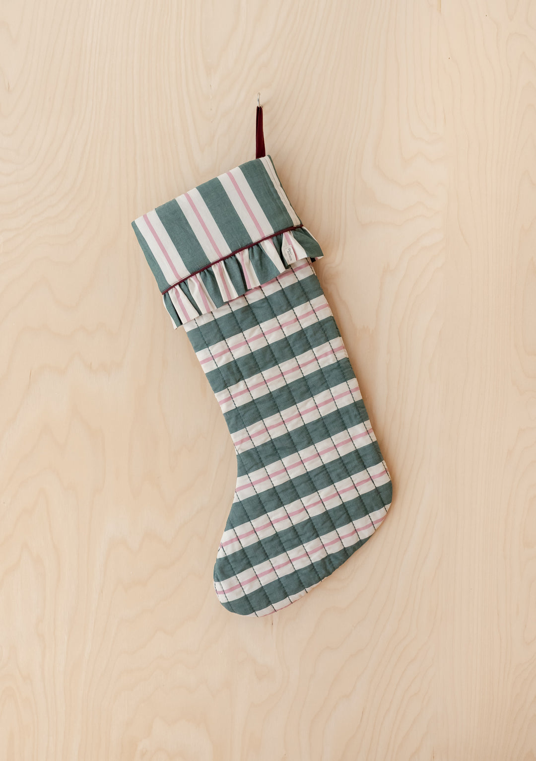 TBCo x Glassette Quilted Cotton Christmas Stocking in Green Stripe hanging, featuring a checkered pattern with ruffle trim, ideal for festive holiday decor.
