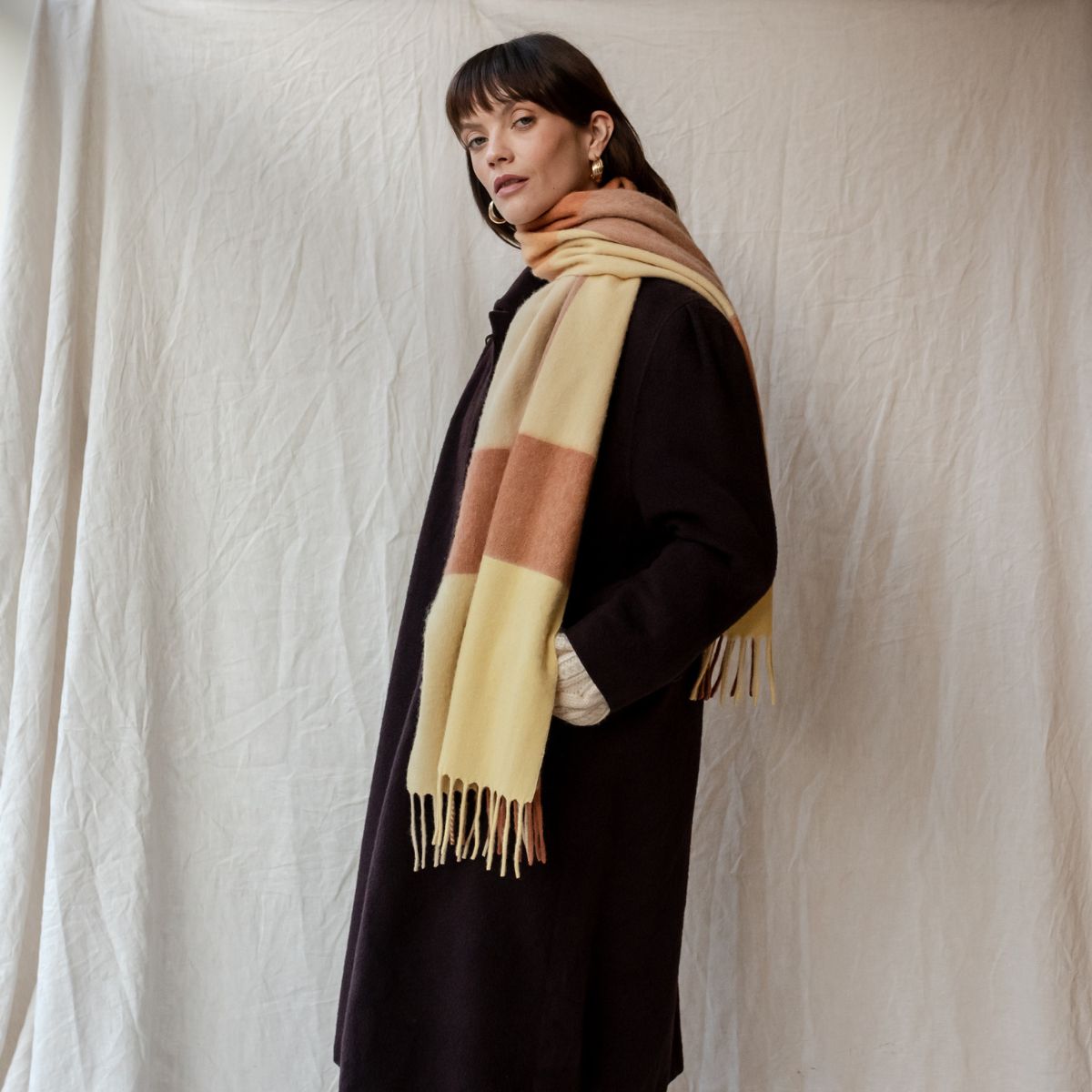 TBCo butter milk and brown lambswool scarf wrapped around the neck, styled with a black wool coat. A soft and elegant winter accessory for timeless layering.