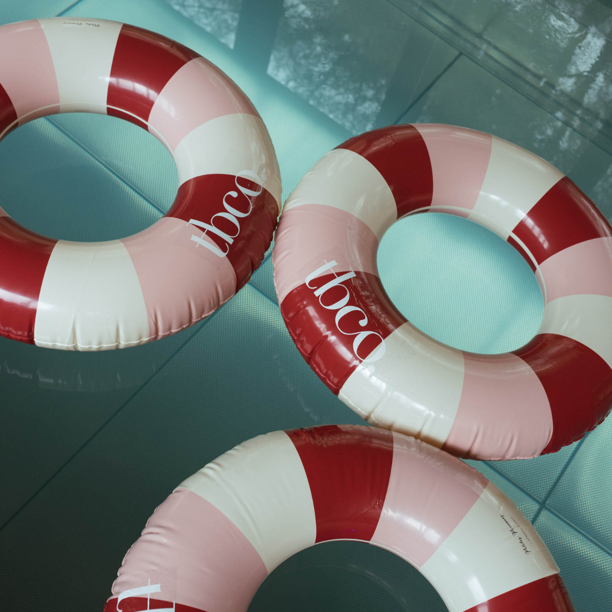 Three  red and white striped TBCo branded pool floats in a blue pool