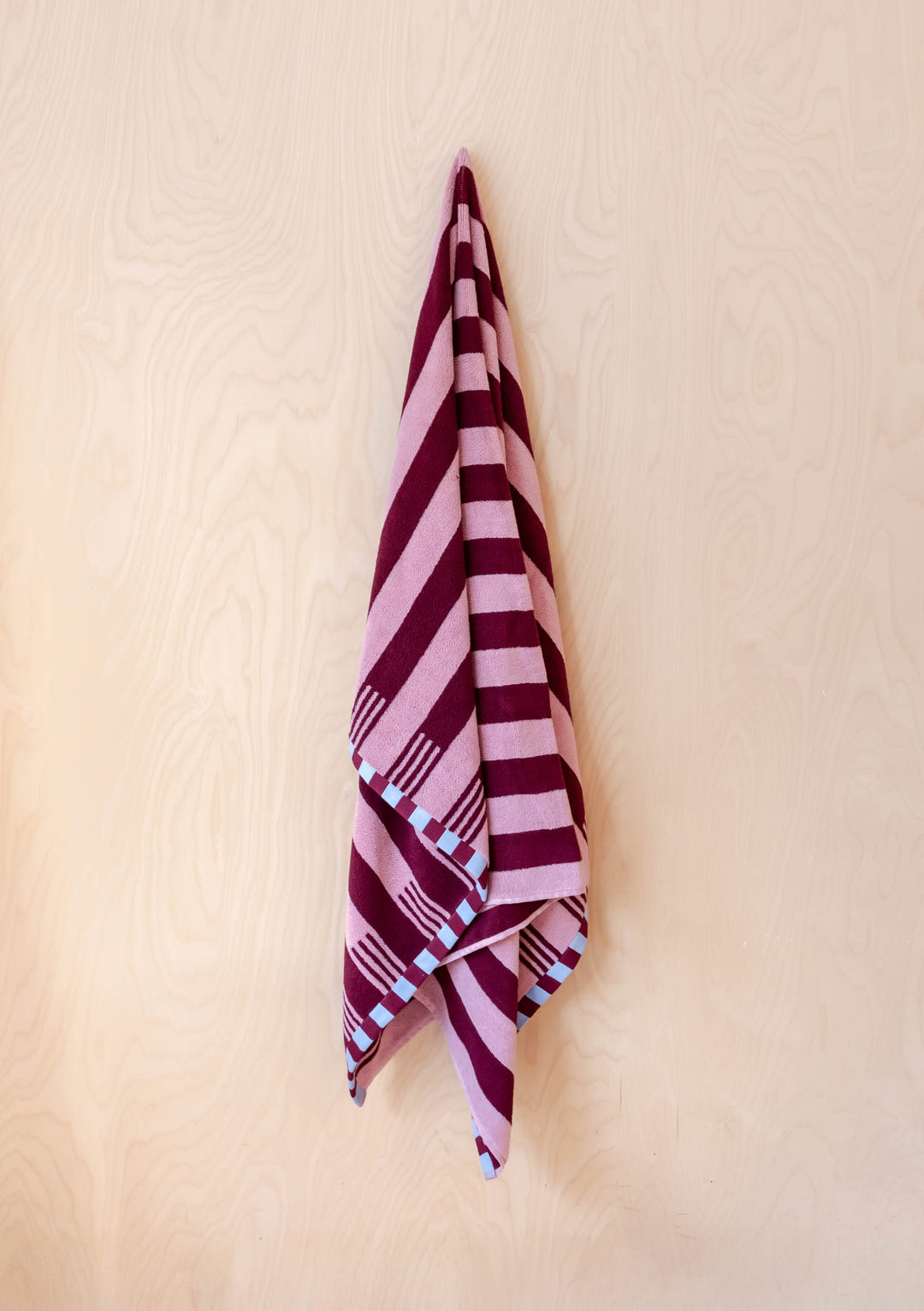 TBCo Terry Cotton Towels in Burgundy Stripe hanging against smooth pale wood wall showing striped pattern and checkerboard edges