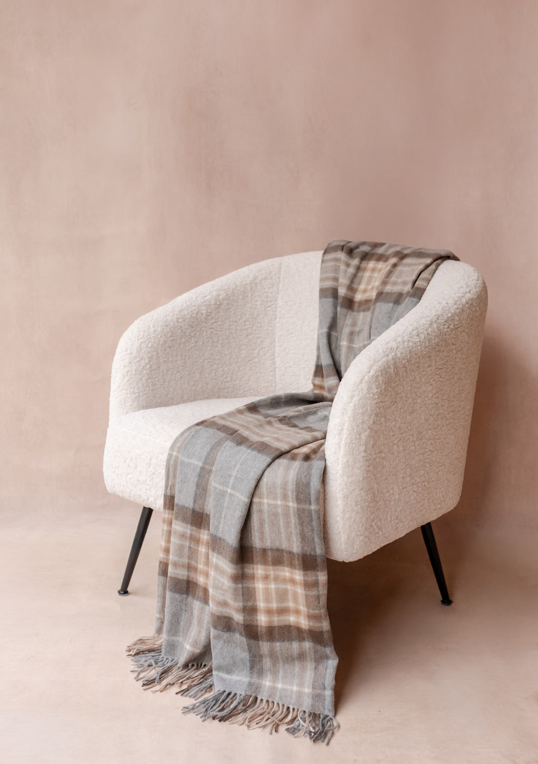 Cashmere Blanket in Mackellar Tartan by TBCo draped over a modern cream armchair with fringed edges.
