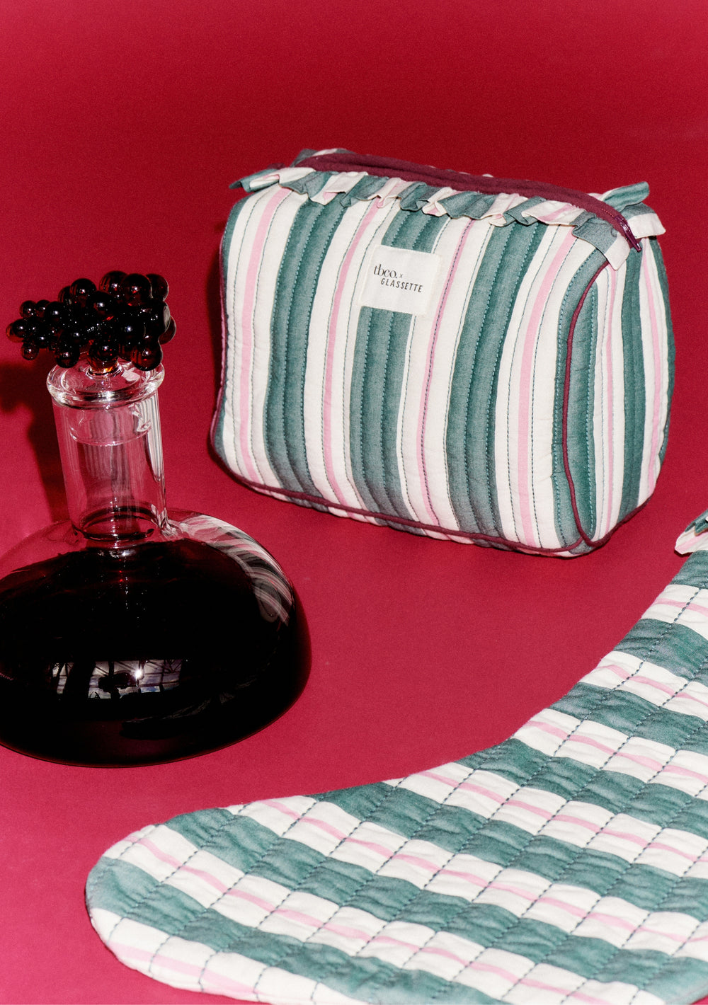 TBCo x Glassette Cotton Wash Bag in Green Stripe, featuring quilted texture, ruffle trim, and zip-top, with matching textile piece and decorative carafe nearby.